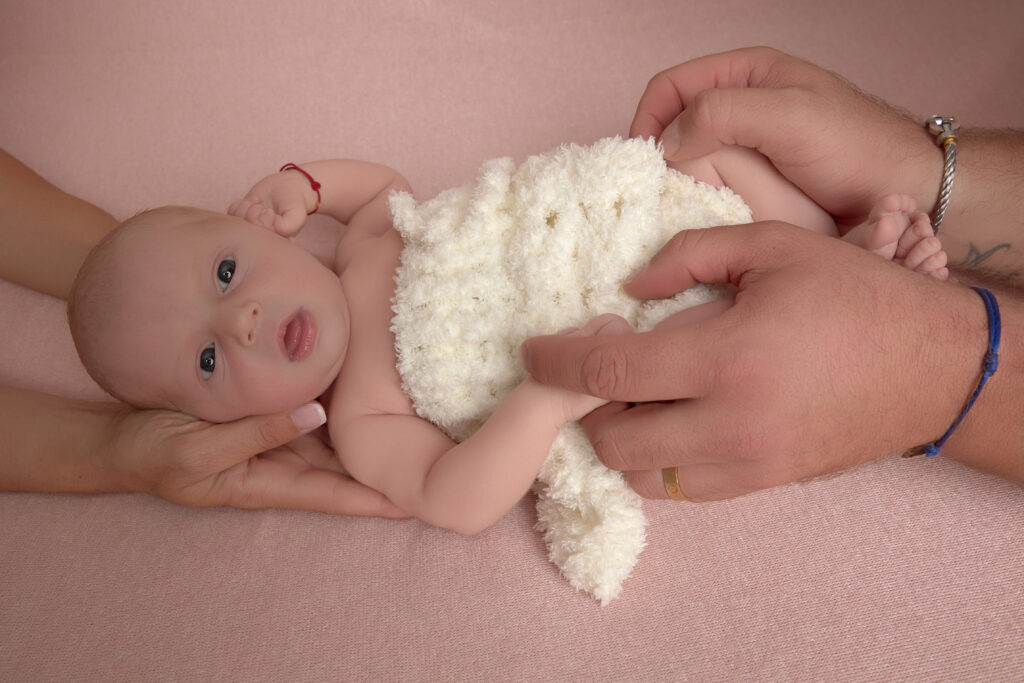 Séance photo newborn à Lavérune près de Montpellier : nouveau-né tenu dans les mains de ses parents, enveloppé dans un tissu tricoté blanc